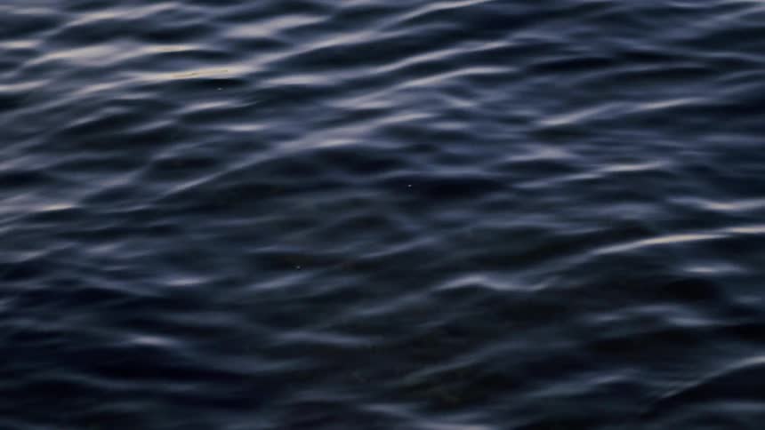 A serene close-up of dark water with gentle, hypnotic ripples moving slowly across the surface