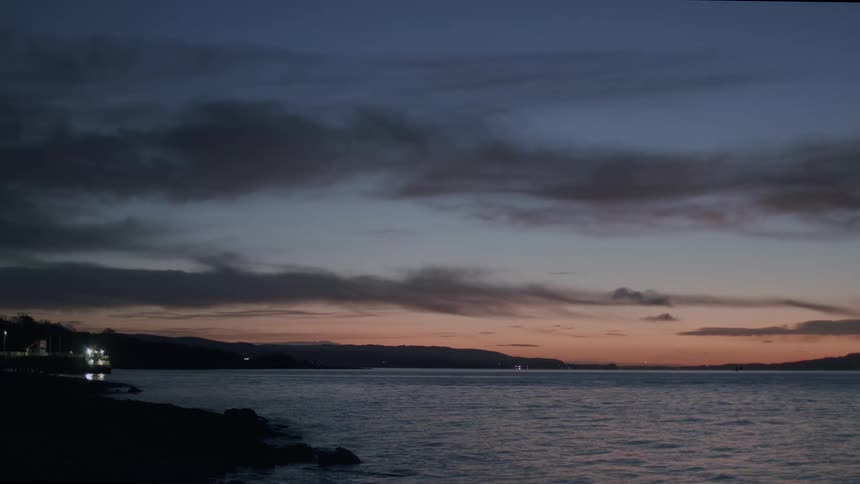 A tranquil coastal scene at twilight, with the last colors of sunset glowing on the horizon over calm water