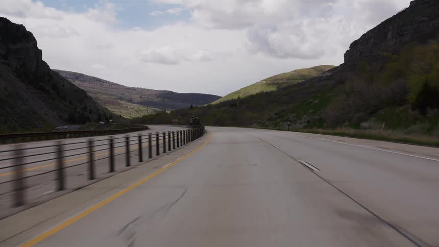 A point-of-view driving shot along a winding mountain highway through a scenic canyon under a cloudy sky