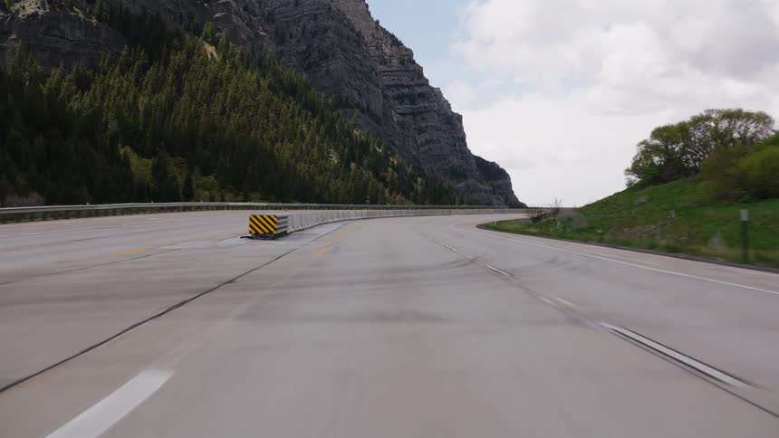 A smooth forward tracking shot captures the point of view of driving along an empty, curving highway through a scenic mountain pass