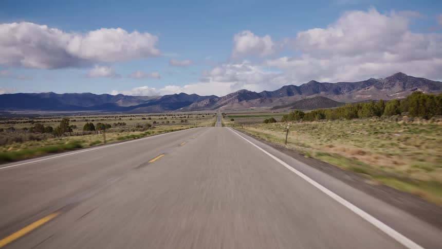 A point-of-view shot driving down a long, straight highway through a vast valley towards distant mountains