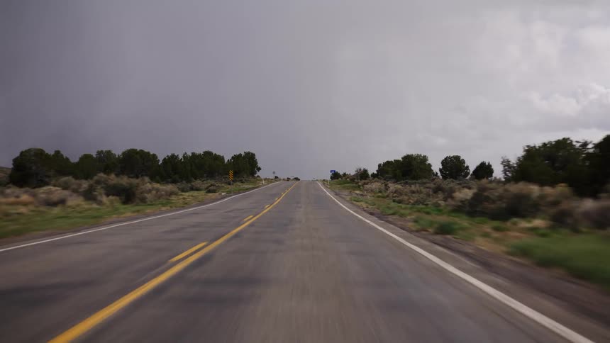 A point-of-view perspective driving down a rural two-lane highway under a dark and stormy sky in the desert