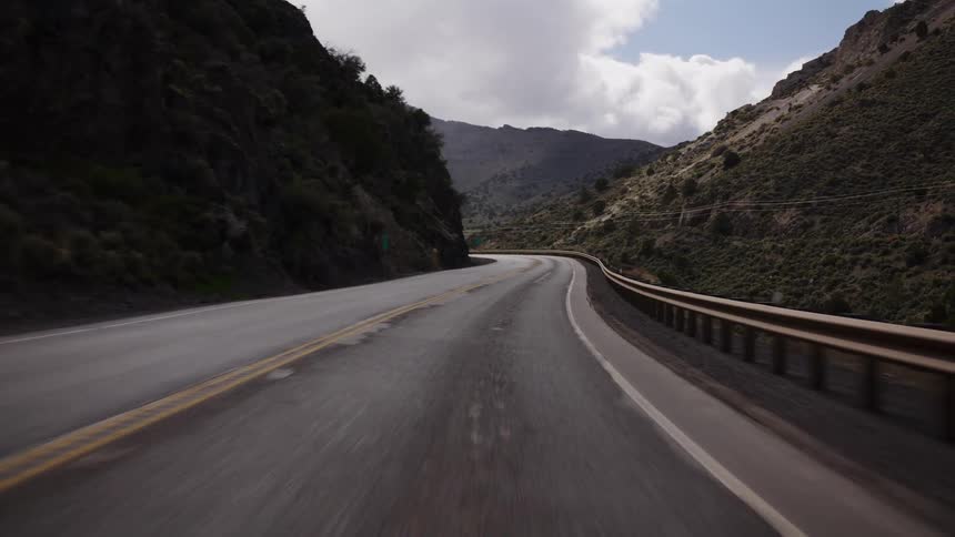 A point-of-view drive on a winding paved road through a rugged mountain canyon