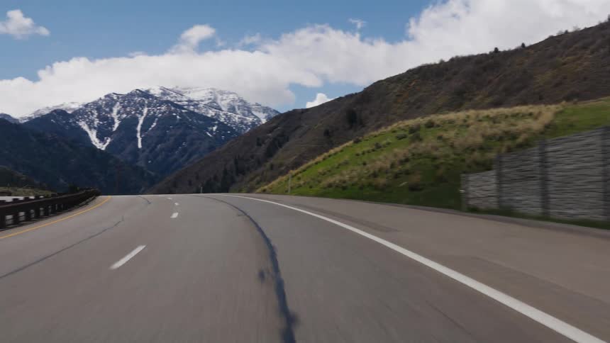 A point-of-view shot driving along a scenic curving highway towards beautiful snow-capped mountains