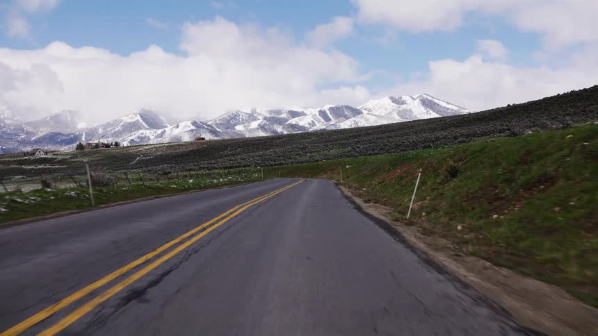 A scenic point-of-view drive on a country road towards a beautiful snow-capped mountain range