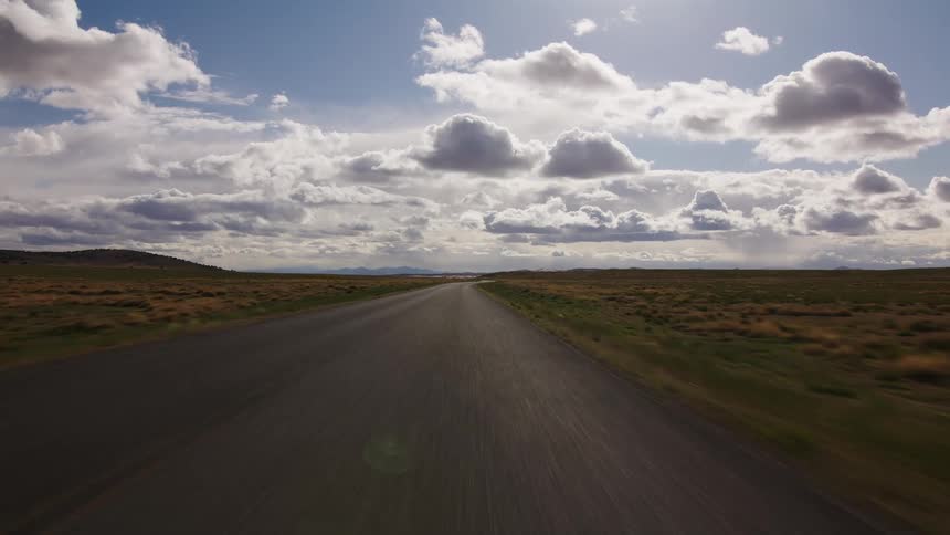 A fast-paced point-of-view drive down a deserted two-lane highway through a wide-open landscape under a cloudy sky