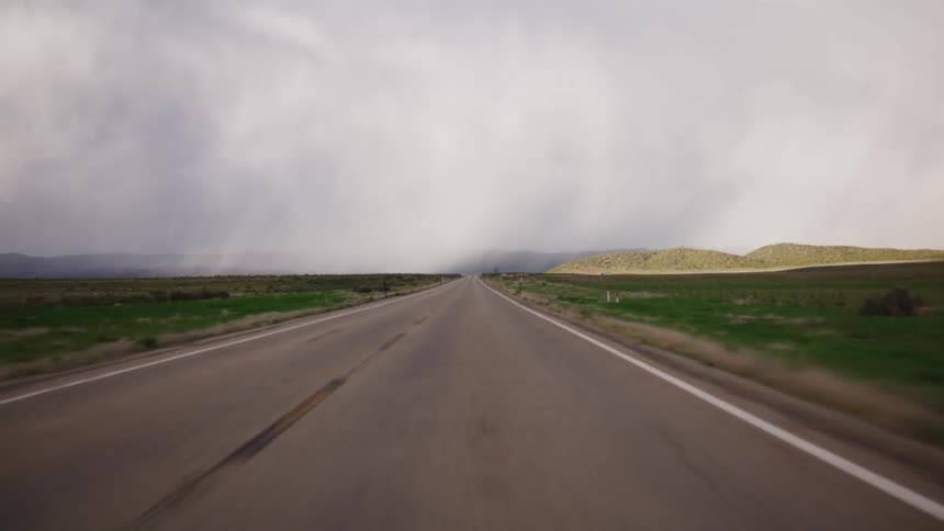 A driver's point-of-view traveling down a long, straight, and empty country road toward a distant storm
