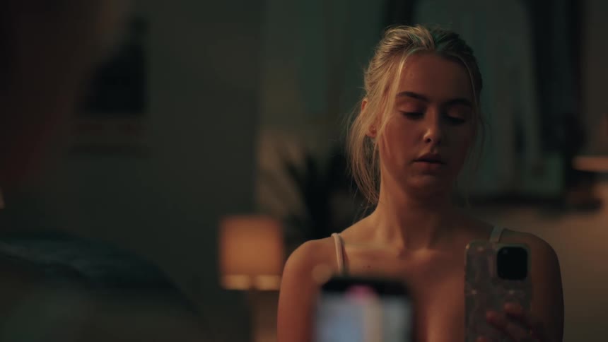 Over the shoulder view of a somber young woman looking at her smartphone in a dimly lit bedroom at night
