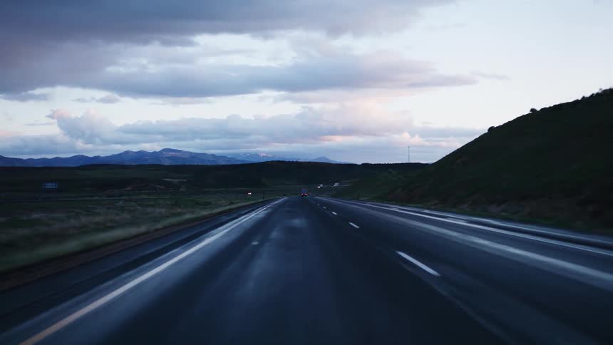 POV driving on a wet highway through a mountain landscape at dusk, tilting up to the overcast sky
