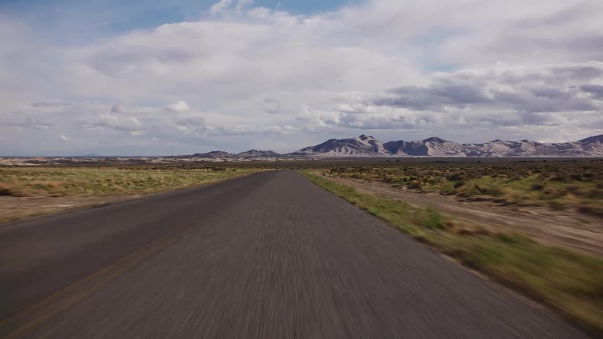 A fast-moving forward view down an empty paved road through the vast desert landscape towards the Little Sahara Sand Dunes in Utah