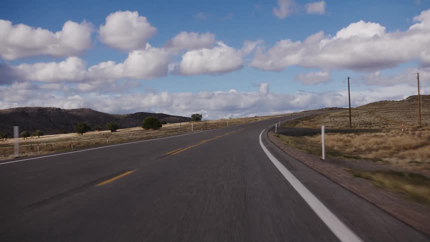Point-of-view driving on a winding desert highway under a beautiful, cloud-filled sky