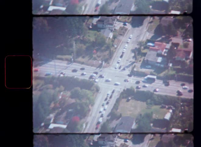 A vintage, shaky aerial shot shows traffic moving through a suburban four-way intersection
