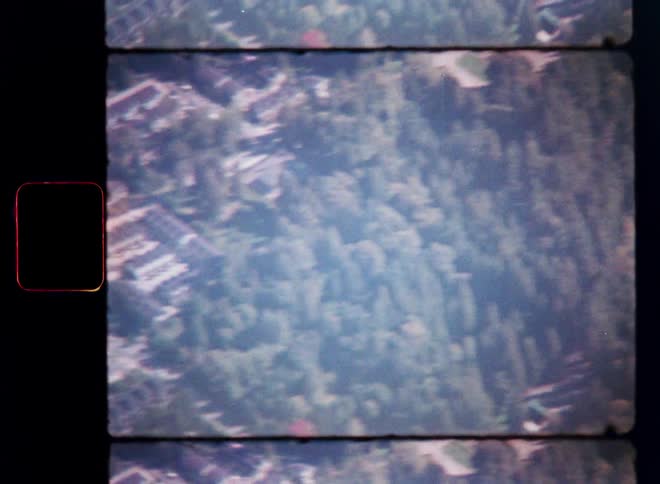 Vintage 8mm film captures a blurry aerial flyover from a suburban neighborhood to a dense, green forest