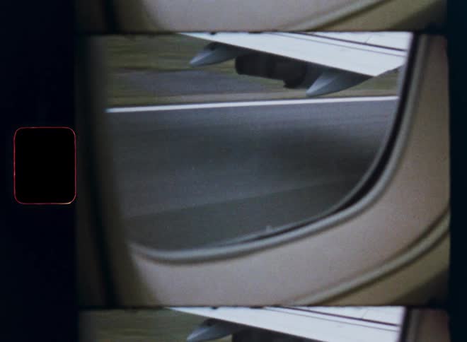 Vintage film with visible frame lines captures the view from an airplane window as it speeds down the runway