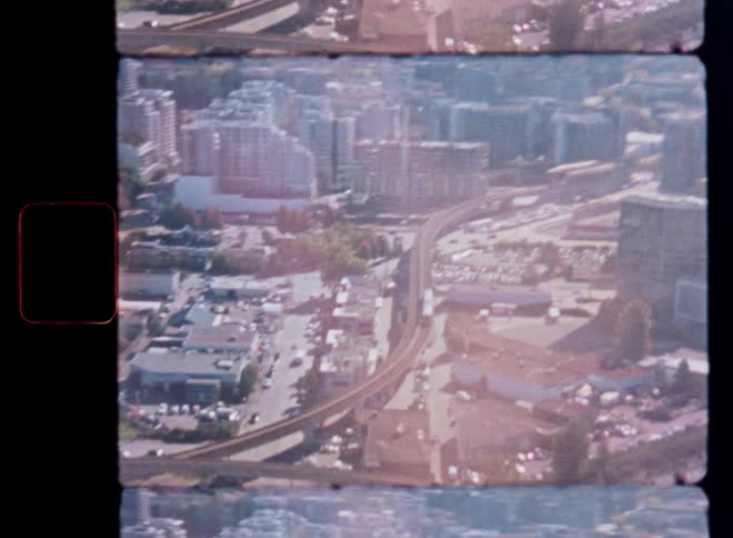 An 8mm vintage aerial shot shows a train traveling on an elevated track through a bustling city during the day