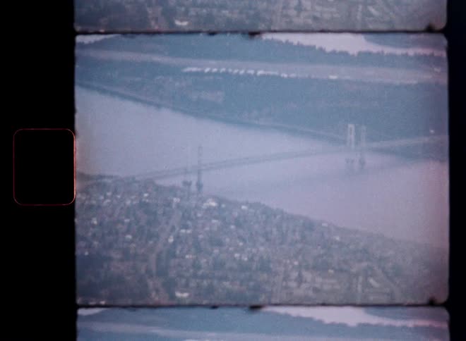 Vintage 8mm film captures a hazy, high-angle aerial view of the Tacoma Narrows Bridge in Washington