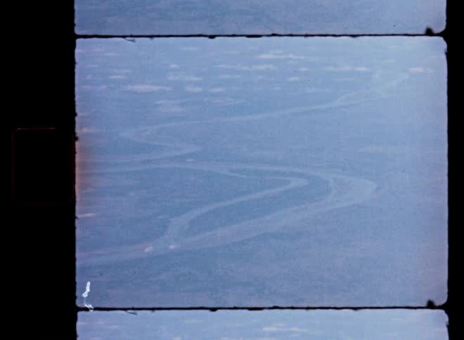 Vintage 8mm film captures a hazy, high-altitude aerial view of a massive meandering river winding through the vast landscape below
