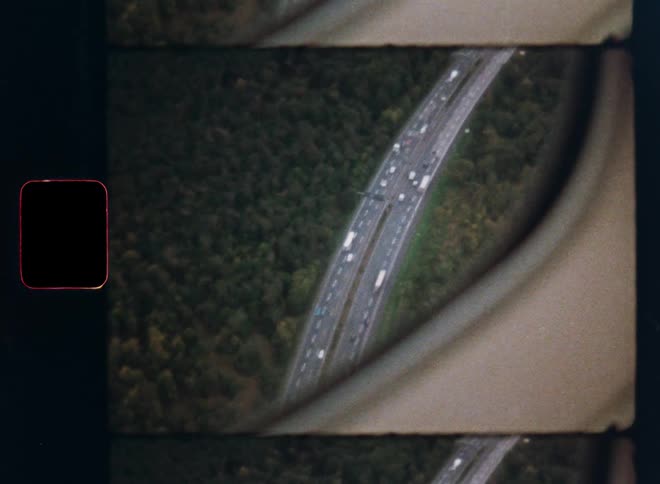 Vintage 8mm film captures a grainy aerial view from an airplane window of a busy highway cutting through a dense green forest