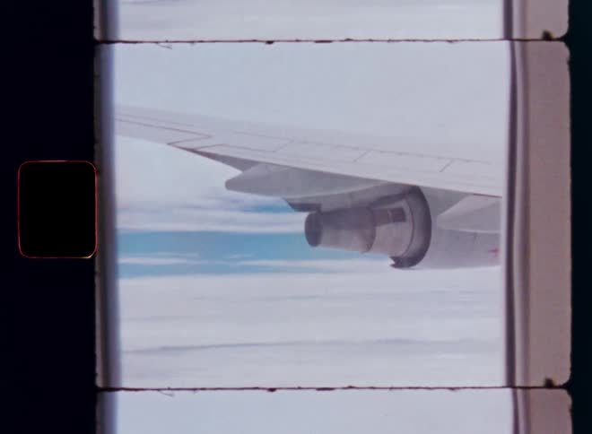 A vintage 8mm film scan shows the view from an airplane window, looking at the wing and engine flying high above the clouds