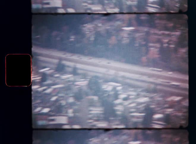 An aerial view from vintage film shows traffic moving along a highway through a suburban neighborhood with autumn trees