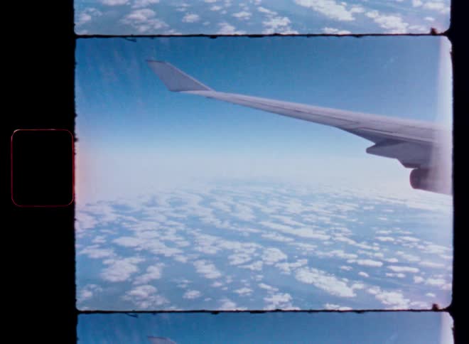 Authentic 8mm film captures an aerial view from an airplane window, showing the wing flying high above a field of white clouds