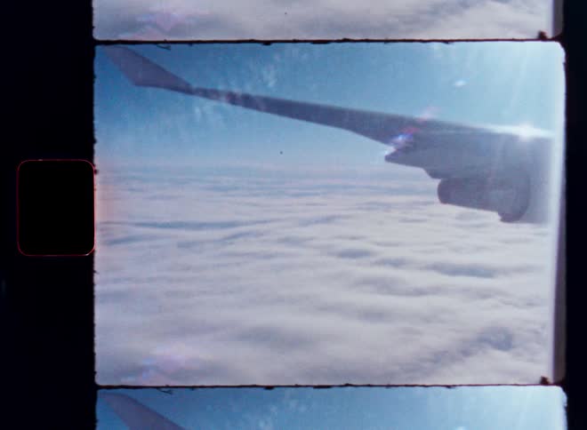 A nostalgic film-style view from an airplane window shows the wing gliding serenely above a blanket of clouds under a bright blue sky
