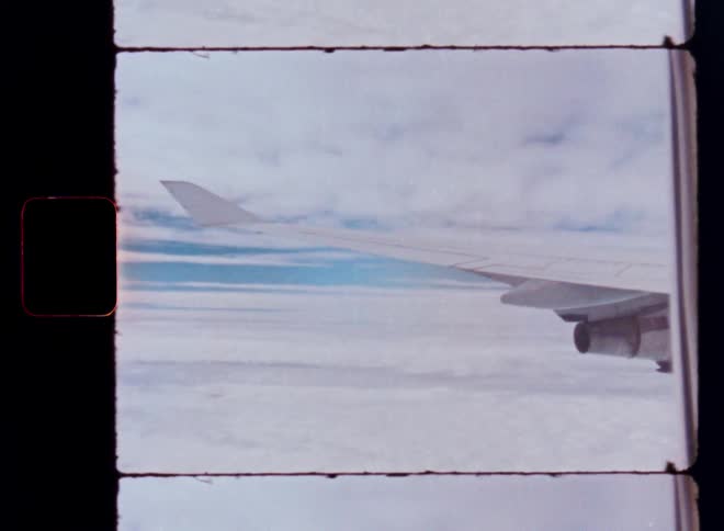 A vintage film shot from an airplane window captures the wing soaring over a vast sea of clouds