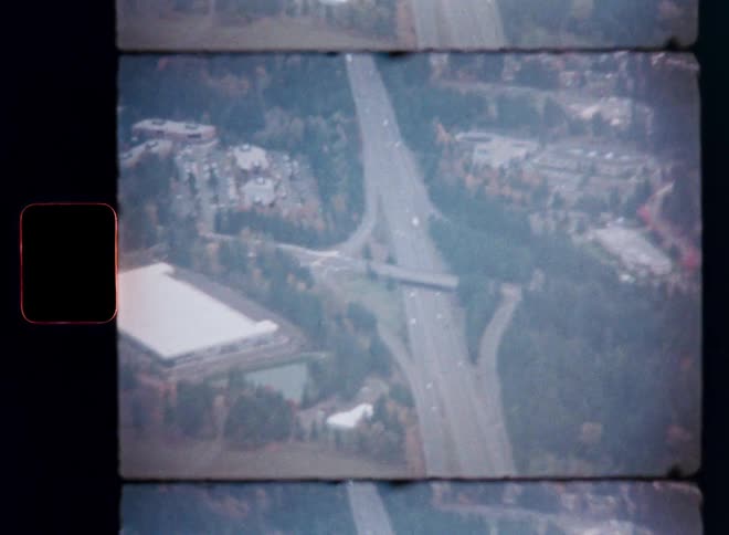 A vintage 8mm film captures an aerial view of a busy highway intersection surrounded by trees