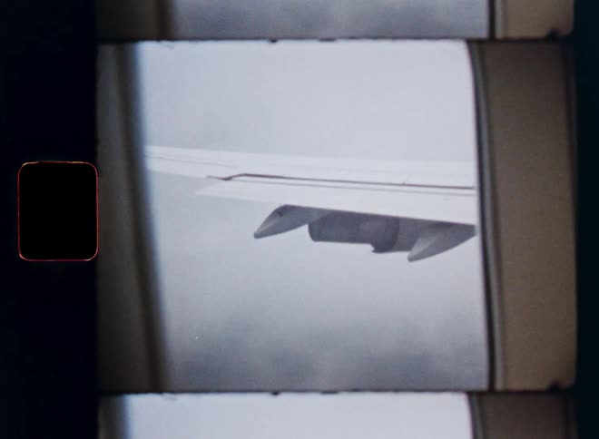 Nostalgic 8mm film captures the view of an airplane wing flying through a cloudy sky