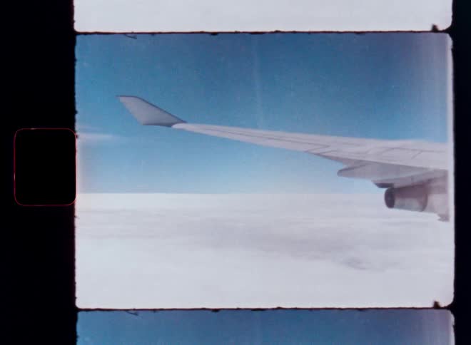 Vintage Super 8 film captures a view from an airplane window, showing the wing and engine flying above a sea of clouds