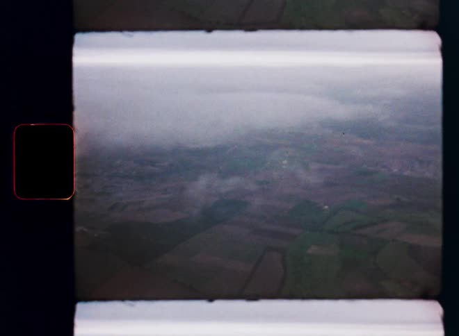 Vintage 8mm film captures an aerial view of a patchwork countryside landscape through the clouds on an overcast day