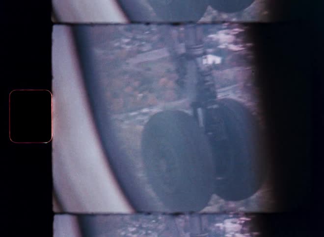 Vintage 8mm film shows an aerial view of a city from an airplane window, with the landing gear in focus as the plane descends for landing