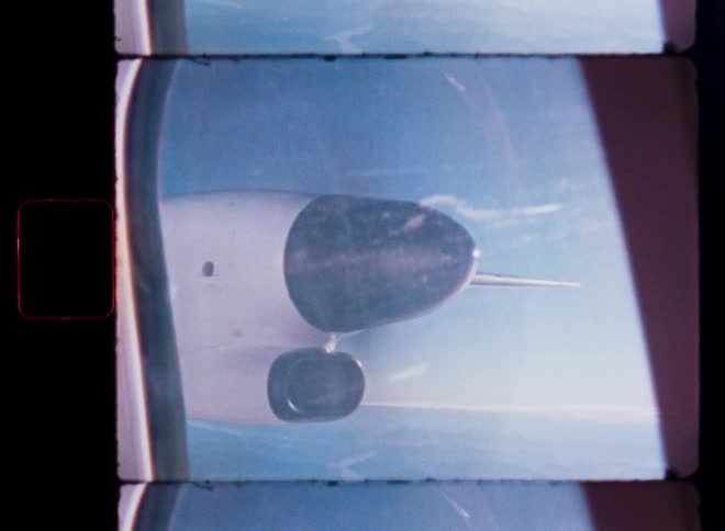 A vertical, vintage Super 8 film view from an airplane window shows the wing and engine flying high over the ocean on a sunny day