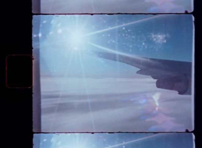 Vintage 8mm film captures an airplane wing soaring above a sea of clouds as the sun creates a beautiful lens flare