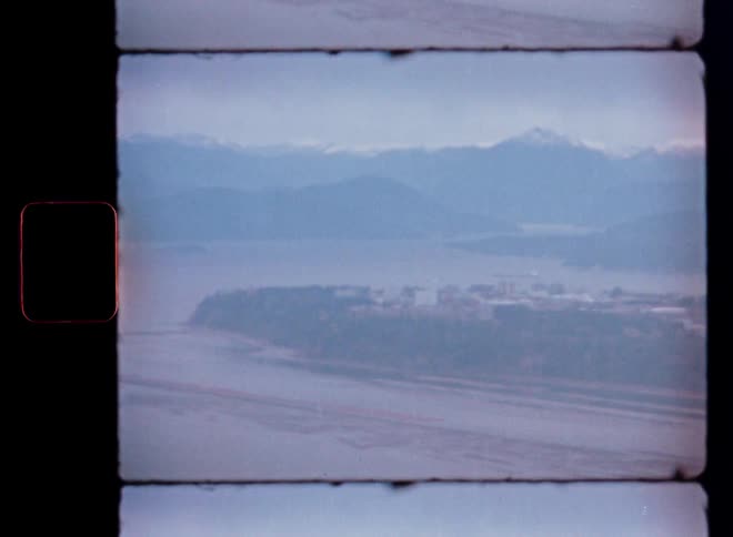 Scanned 8mm film captures a hazy, distant view of a seaside town and snowy mountain range