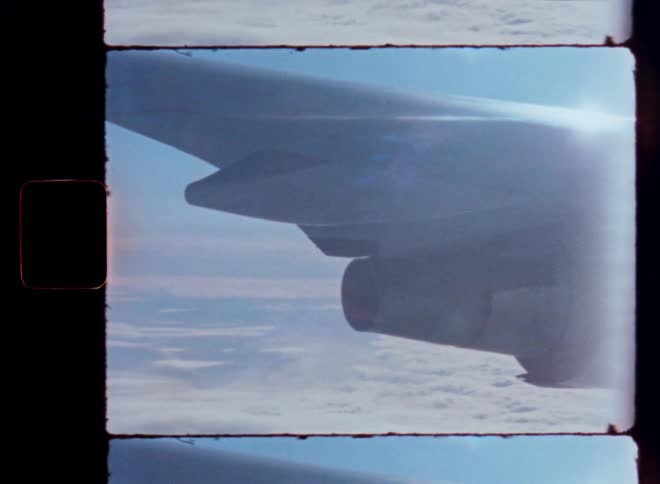 A vintage film shot from an airplane window shows the wing and engine flying high above a sea of clouds