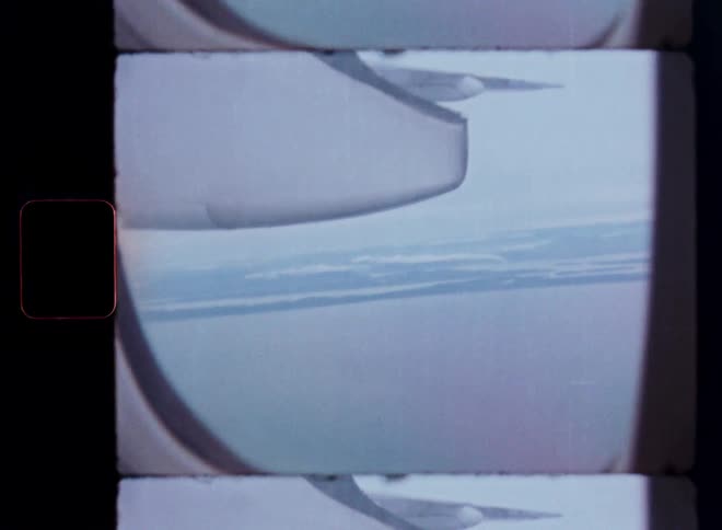An authentic vintage 8mm film scan shows the view from an airplane window, with the wing visible as it flies over a vast body of water and land