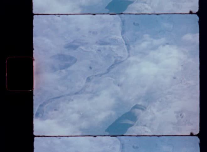 A grainy archival shot from space reveals the Earth's majestic, cloud-dusted landscape slowly passing below
