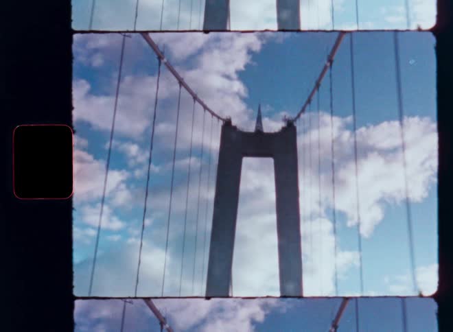 Vintage 8mm film strip captures a dreamy, abstract view of a suspension bridge tower against a cloudy blue sky