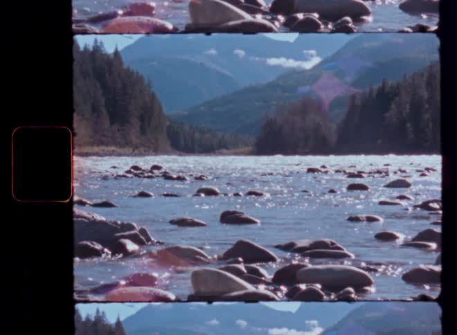 A vintage Super 8mm film captures a tranquil river flowing through a rocky bed with a mountain forest in the background