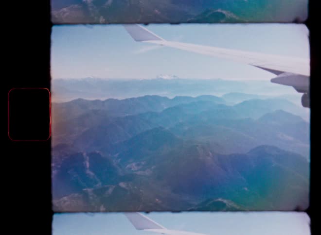 Vintage 8mm film footage of a hazy mountain range seen from an airplane window