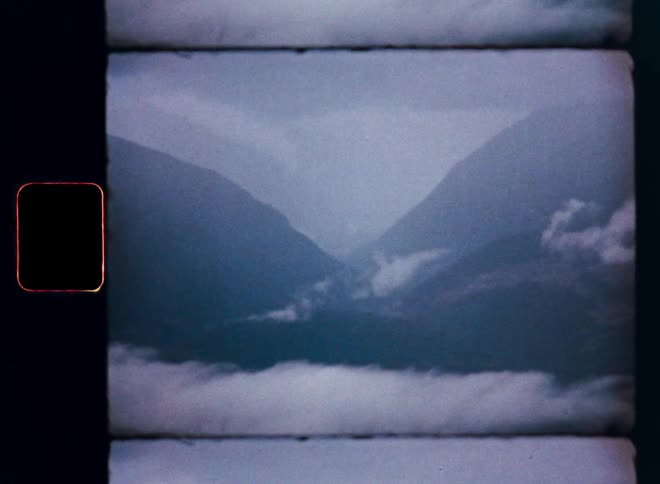 Archival film footage captures a moody, atmospheric shot of a misty mountain valley enveloped in low-hanging clouds