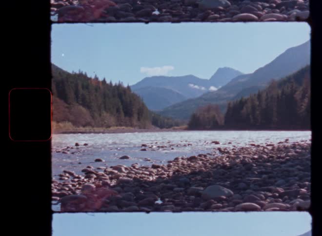 A vintage film still captures the scenic view of a rocky river flowing through a mountain valley