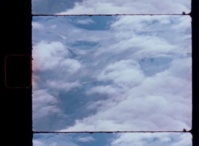 A vintage film frame captures a serene view of clouds floating over a majestic mountain range