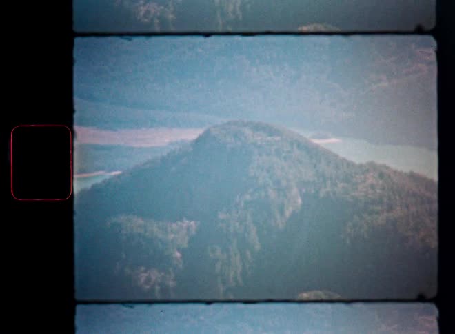 Vintage film scan captures an aerial view of a lush, tree-covered mountain landscape with a river in the background