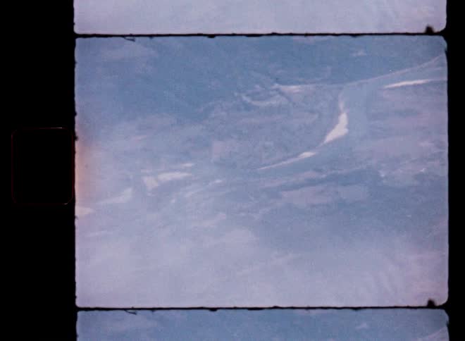 Vintage 8mm film captures a hazy aerial view of a winding river through a mountainous landscape
