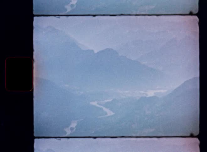 Vintage 8mm film scan shows a hazy, atmospheric view of a river snaking through a mountainous valley