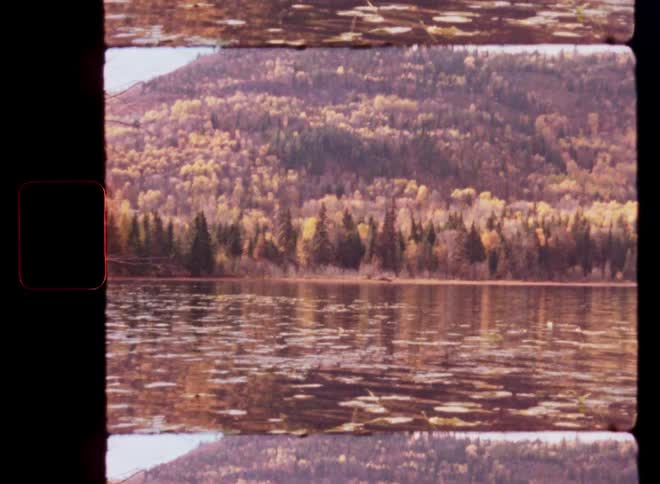Archival 8mm film captures a peaceful autumn lake scene with a colorful forest in the background