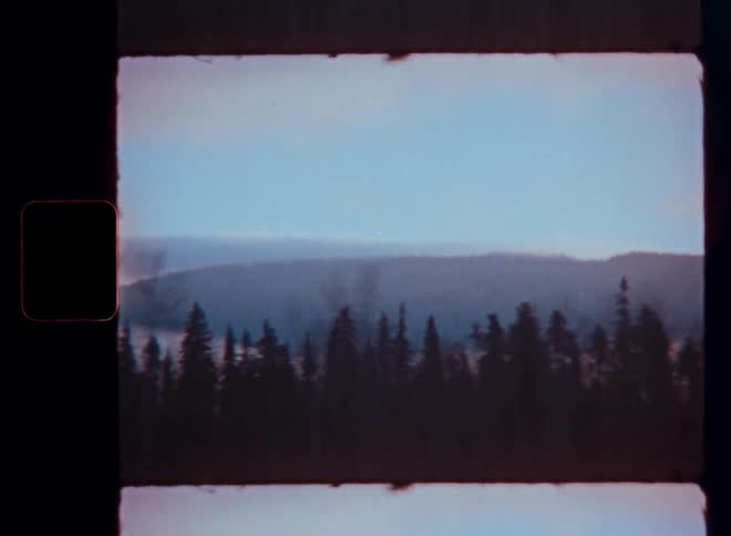 A dreamy, passing landscape of a silhouetted forest against hazy mountains, captured on vintage 8mm film