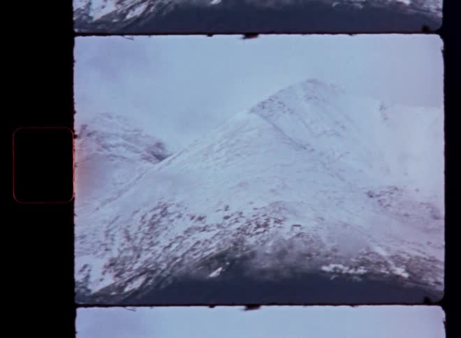 Archival film scan of a majestic, snow-covered mountain peak shrouded in clouds